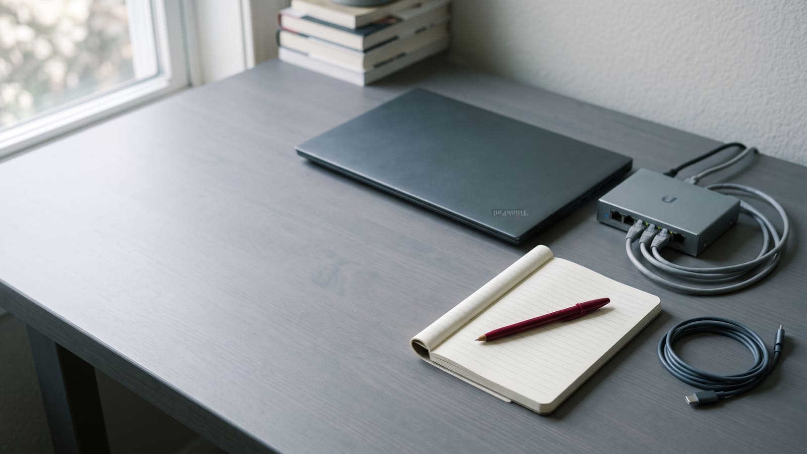 A tidy desk with a closed laptop, a small network switch, coiled cabling and a notebook.
